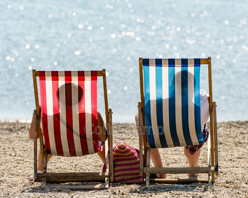 Deckchairs 
 Traditional beach seaside scene as a couple sit in red and white and blue and white deckchairs facing the sea and enjoying the sun. 
 Keywords: Southend coast his n hers summer deckchairs seaside beach seaside